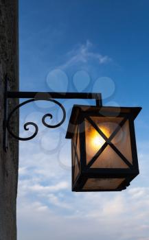 Ancient street lamp mounted on stone wall over dark blue sky background