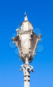 Old style white street lamp with wrought iron decoration over blue sky background
