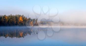 Calm lake panoramic landscape with fog in cold autumn morning