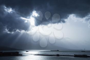 Dark dramatic sky with sunlight rays over sea. Blue toned photo filter effect