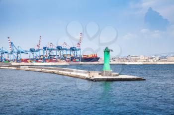 Port of Naples, cityscape with container cranes and green lighthouse on concrete breakwater