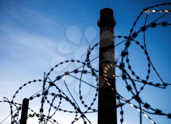 Barbed wire and dark tall industrial chimney-stalk shilouette