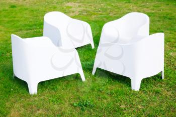 Four modern white plastic chairs stand on fresh green grass
