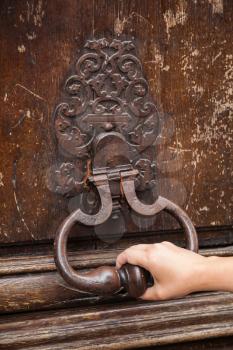 Hand and old rusted knocker on brown wooden door in Paris, France
