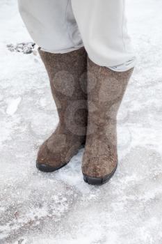Feet with traditional Russian gray felt boots stand on winter road with snow and ice 
