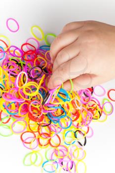 Little child hand and pile of small round colorful rubber bands for making rainbow loom bracelets on white background