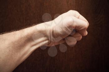 Strong male fist over dark brown wooden wall background
