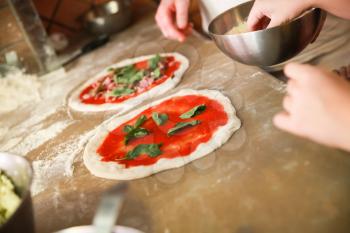 Preparing Pizza Margherita, the archetype of Neapolitan pizza. Cooks adds grated parmesan cheese. Selective focus