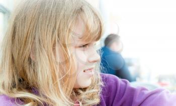 Closeup profile portrait of a little blond girl above light city background