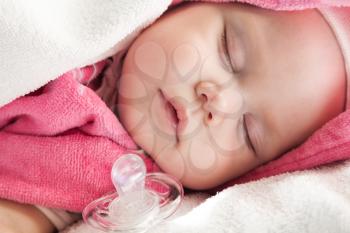 Baby girl sleeps in pink and white cotton towels with a pacifier nearby;