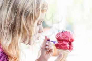 Little girl eats big ice-cream in the park. Profile portrait with selective focus