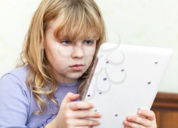 Cute little blond girl using white tablet computer
