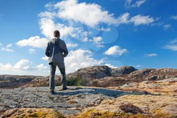 Young man stands on the rock and looks over horizon