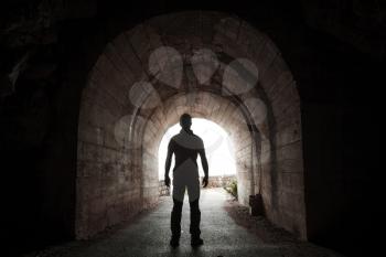 Young man stands in dark tunnel and looks out in the glowing end