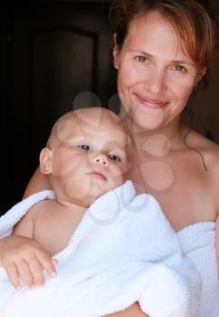Young Caucasian mother with her baby in white cotton towel after the bath