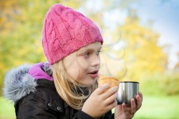 little beautiful blond girl eating cake with tea in autumnal park. Outdoor portrait.