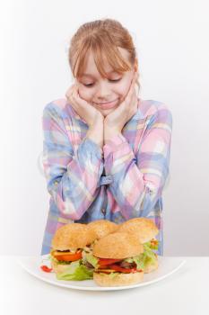Little smiling blond girl looks on homemade hamburgers on white plate