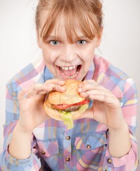 Little blond smiling girl eats hamburger above white wall