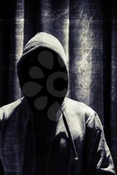 Portrait of incognito man under hood with grunge curtain background