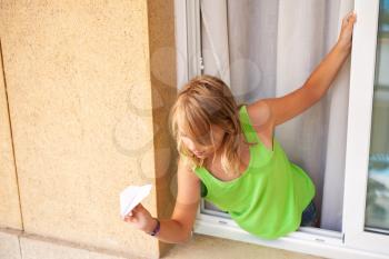 Little blond Caucasian girl with paper plane in the window