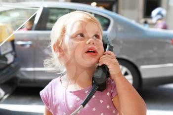 Outdoor portrait of little Caucasian blond girl talking on the street phone