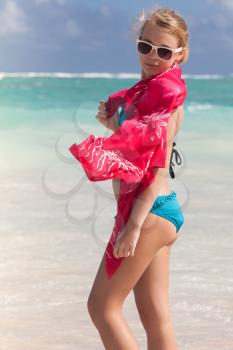 Outdoor portrait of beautiful Caucasian girl in blue swimsuit and red shawl standing on the coast