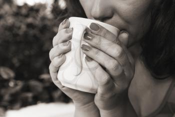 Woman hold white cup of coffee in her hands. Closeup black and white outdoor photo