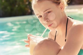 Little blond girl drinks cocktail in swimming pool, vintage toned photo with filter effect