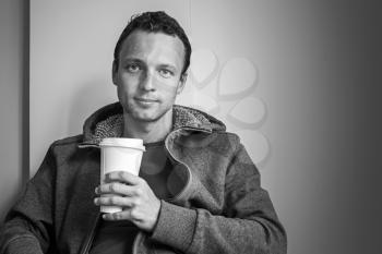 Portrait of young Caucasian man sitting in cafe with paper cup of Coffee. Black and white photo