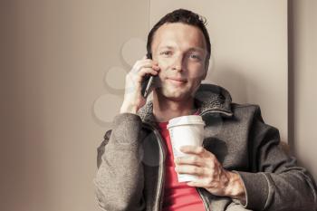 Portrait of young Caucasian man sitting in cafe with paper cup of Coffee. Vintage toned photo effect