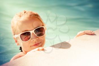 Beautiful little blond girl with sunglasses in outdoor pool, closeup summer portrait, toned photo, old style filter effect