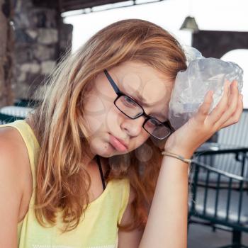 Blond Caucasian teenage girl puts ice to the head