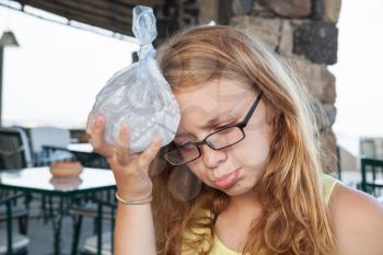 Blond Caucasian teenage girl puts ice in a plastic bag to the head