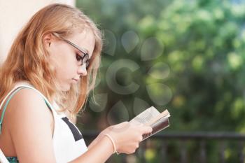 Blond Caucasian teenage girl sits on the balcony and read a book