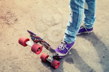 Teenager feet in blue jeans and gumshoes on a skateboard, photo with warm retro tonal correction, old style