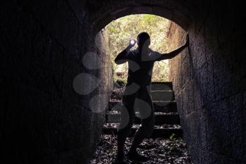 Young man with flashlight enters dark stone tunnel and looks inside, tonal correction photo filter effect