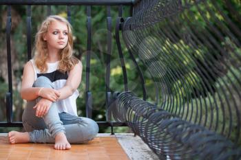 Beautiful blond Caucasian girl sits on balcony, outdoor summer portrait