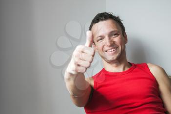 Positive young smiling Caucasian man shows thumbs up gesture, studio portrait