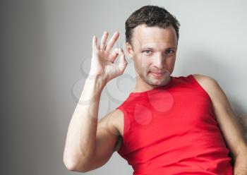 Positive young smiling man in red shirt shows okay gesture