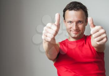 Positive young smiling Caucasian man shows thumbs up, studio portrait