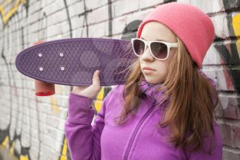 Teenage girl holds skateboard near by urban wall with graffiti