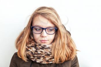 Closeup portrait of beautiful blond Caucasian teenage girl in glasses and warm scarf over white wall background