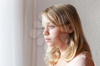 Closeup portrait of beautiful blond Caucasian girl near a window with white curtains