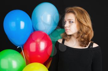 Closeup studio portrait of beautiful teenage blond girl with colorful balloons over black background