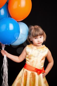 Vertical studio portrait of cute Caucasian blond little girl with colorful balloons