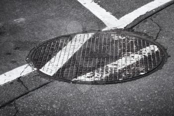 Round sewer manhole on asphalt road with white marking lines
