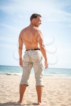 Barefoot sporty man stands on sandy summer beach