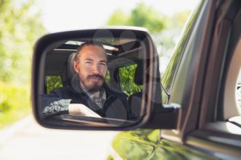 Serious Asian man as a driver looks in car mirror, outdoor summer portrait 