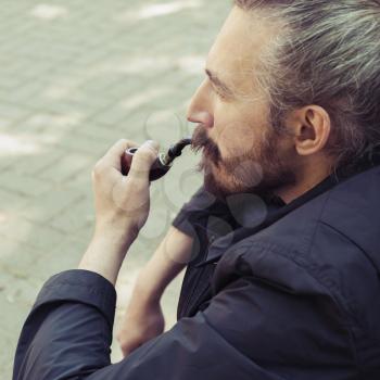 Bearded man smoking pipe, square outdoor portrait with selective focus and vintage tonal correction photo filter, old style effect