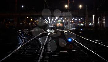 Railroad night scene with blue traffic light and cargo trains. Selective focus on semaphore